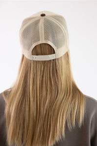 Back view of a person with long blonde hair wearing a beige mesh trucker cap with an adjustable strap, set against a plain white background.