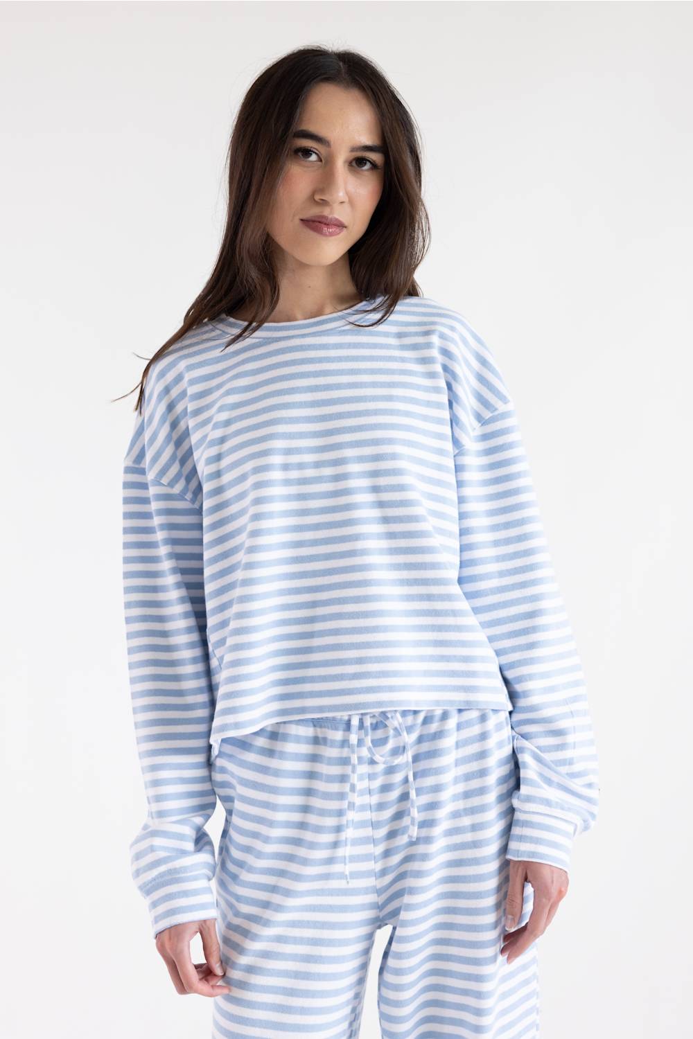 A woman modeling a light blue and white striped long-sleeve top and matching striped pants against a plain white studio background.
