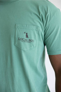 A close up of a light green shirt with a graphic saying Local Boy Outfitters with a dog and a half moon.