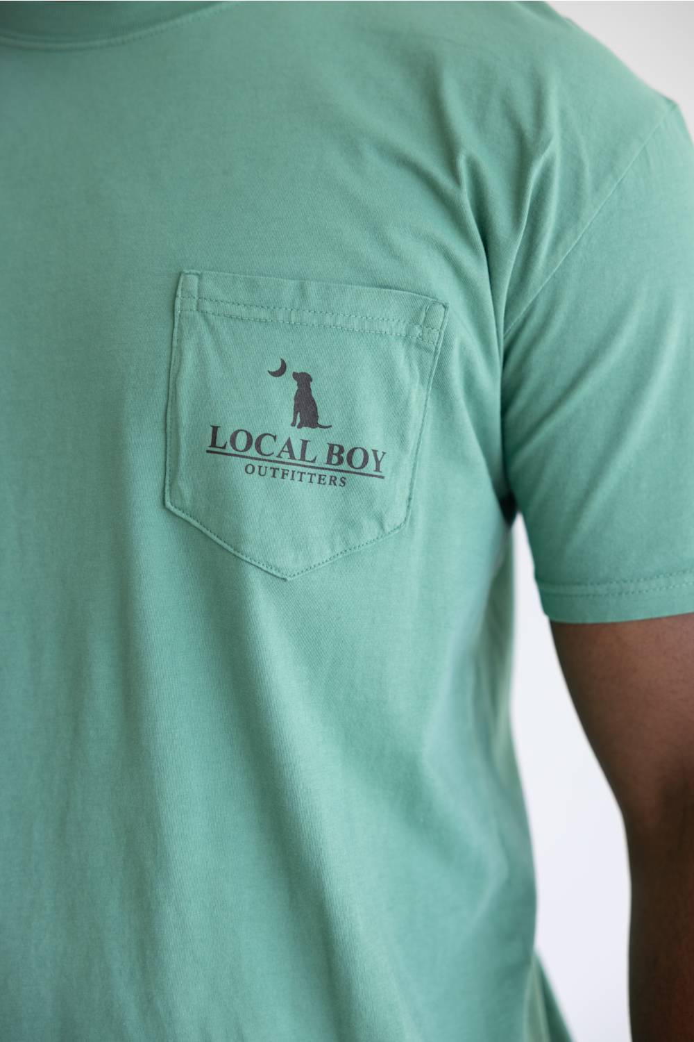 A close up of a light green shirt with a graphic saying Local Boy Outfitters with a dog and a half moon.