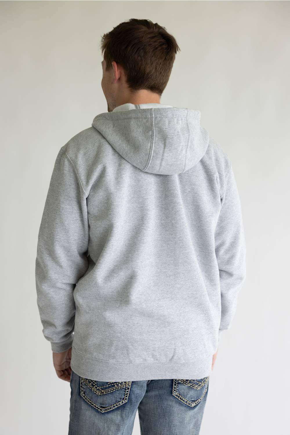 A person viewed from the back wearing a light gray heather pullover hoodie and blue jeans against a plain light background.