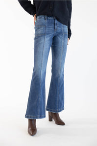 A model from the waist down wearing medium-dark wash blue flare jeans, a dark navy cardigan, and brown ankle boots, standing against a plain white studio background.