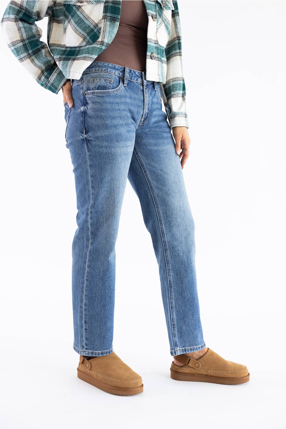 A person wearing light blue straight-leg denim jeans, styled with a green and white plaid flannel shirt and tan suede slip-on shoes against a plain white background.