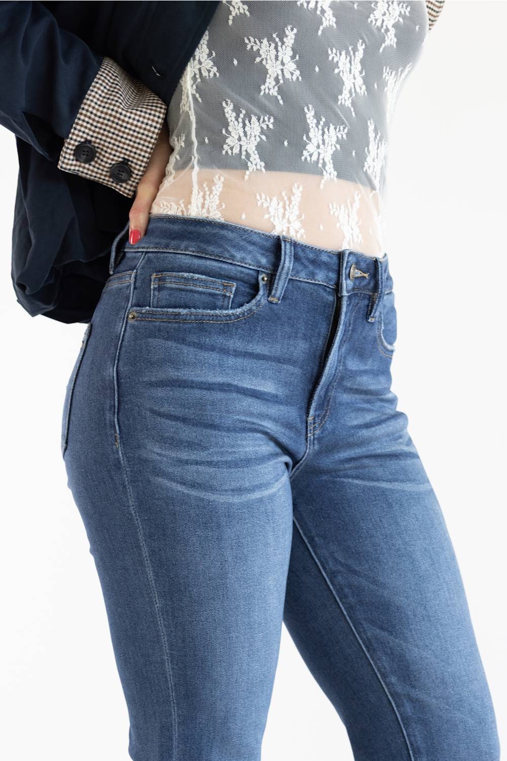 Close up of a model wearing a pair of dark-wash blue straight-leg jeans, styled with a white lace top, and a dark navy jacket set against a plain white studio background.