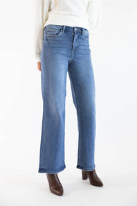 A person wearing medium-wash blue wide leg jeans with a white ribbed sweater and brown heeled ankle boots, shown from the waist down against a plain white studio background.