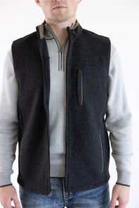 A man wearing a dark charcoal gray zip-up fleece vest over a light gray long-sleeve shirt and blue jeans, shown from the neck down against a plain white background.