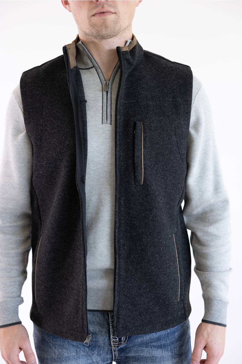 A man wearing a dark charcoal gray zip-up fleece vest over a light gray long-sleeve shirt and blue jeans, shown from the neck down against a plain white background.