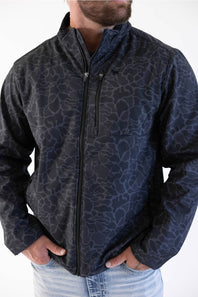 A man wearing a dark navy blue zip-up jacket with a tonal abstract animal-like pattern, paired with light blue jeans, shown from the neck down against a plain white background.