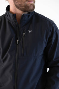 A close-up of a man wearing a dark navy blue zip-up jacket with a small white dog logo on the left chest, set against a plain white background.
