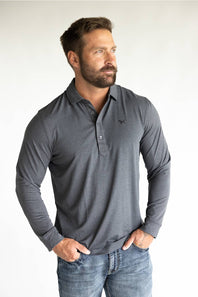 A muscular man wearing a dark gray long-sleeve polo shirt with a small embroidered logo on the left chest, paired with blue jeans, standing against a plain white studio background.