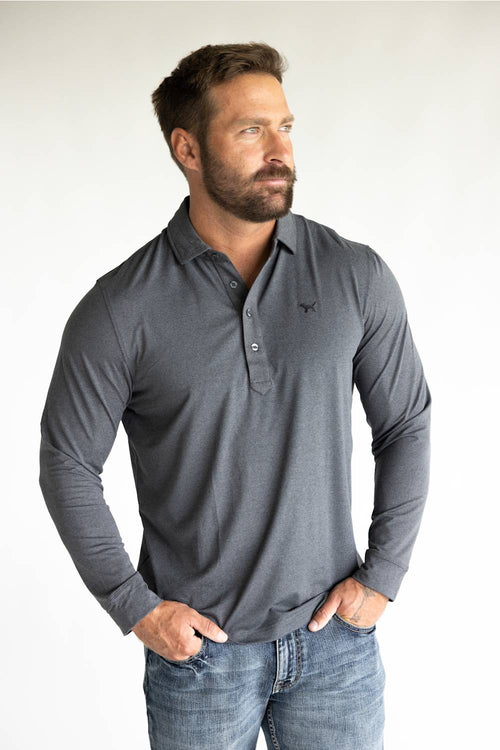 A muscular man wearing a dark gray long-sleeve polo shirt with a small embroidered logo on the left chest, paired with blue jeans, standing against a plain white studio background.