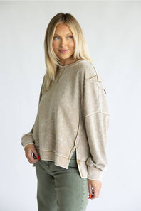 A blonde woman wearing a beige mineral-wash cropped sweatshirt and olive green pants, standing against a plain light gray studio background.