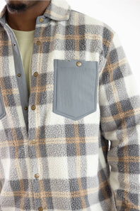 Close-up of a person wearing a sherpa fleece plaid button-up shirt in white, gray, and tan, with a solid gray chest pocket.