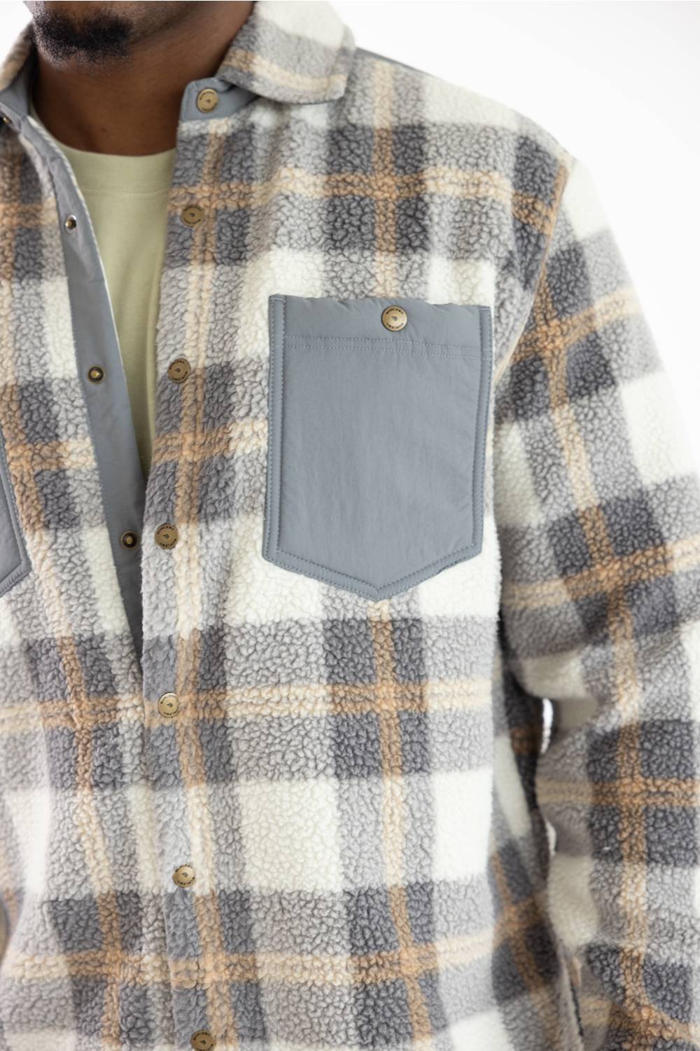 Close-up of a person wearing a sherpa fleece plaid button-up shirt in white, gray, and tan, with a solid gray chest pocket.