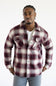 A man wearing a long-sleeve button-up plaid flannel shirt in burgundy and cream, layered over a white t-shirt and gray pants, standing against a plain white background.