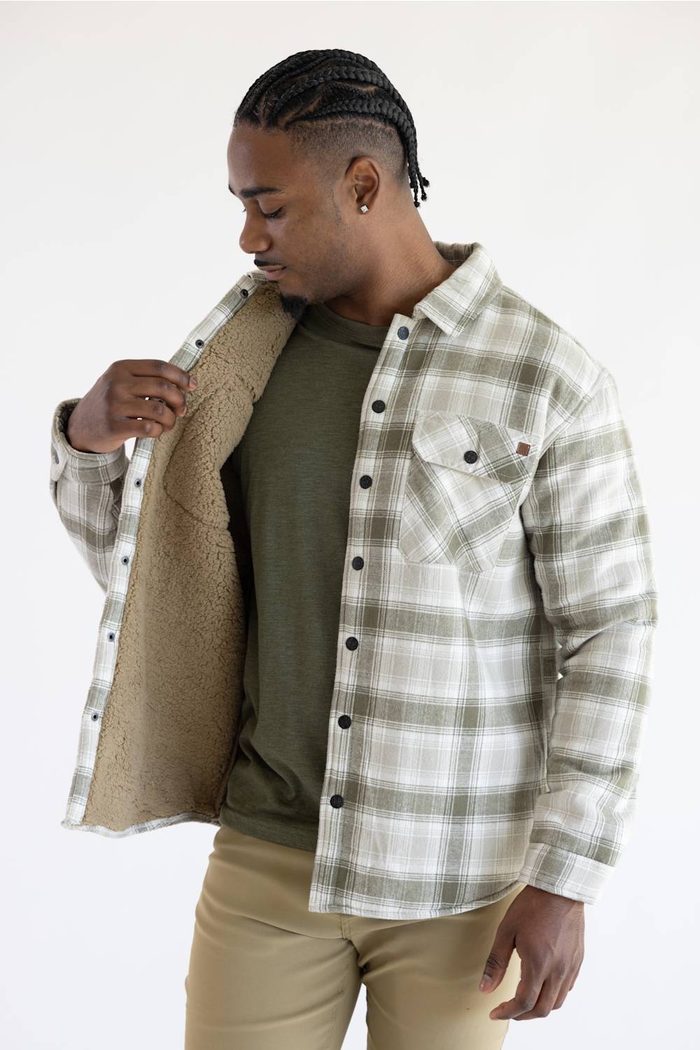 A man wearing a long-sleeve plaid button-up shirt in beige, white, and gray, paired with khaki pants, standing against a plain white studio background.