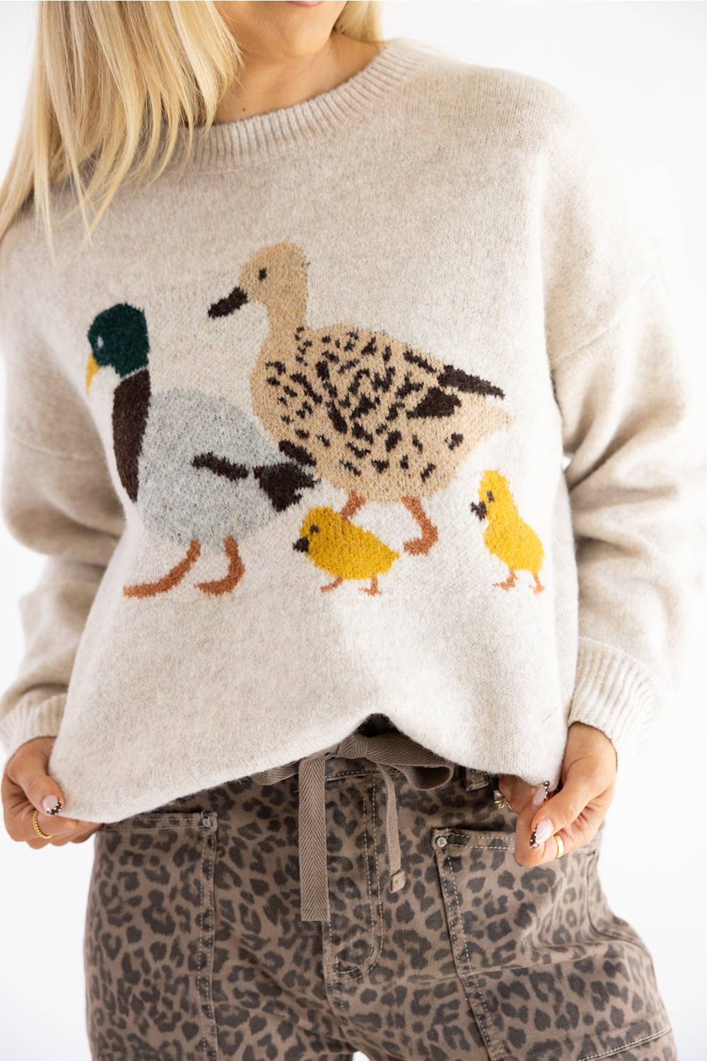 A woman wearing a cream-colored knit sweater with a large embroidered duck family design on the front, paired with leopard-print pants.