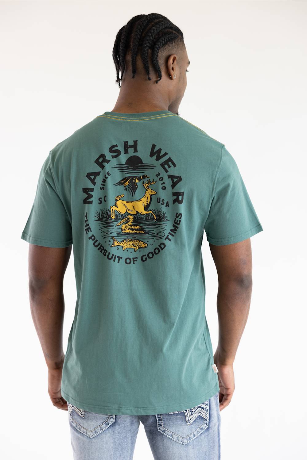 A man viewed from the back wearing a sage green t-shirt with a large yellow and black graphic print on the back that reads 'MARSH WEAR' and 'THE PURSUIT OF GOOD TIMES'.