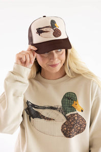 Model wearing the Mallard Duck Trucker Hat for Women in Cream and Brown, featuring a mesh back, brown adjustable snapback brim, and a detailed patch-stitch mallard duck graphic on the front.
