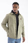 Front-facing studio shot of a model wearing the Marsh Wear Delano Cord Shacket in Sage Brush green corduroy, featuring an embossed leather brand patch on the left chest, antique brass snap closures, and dual side hand pockets, layered over a dark hoodie and styled with blue jeans.
