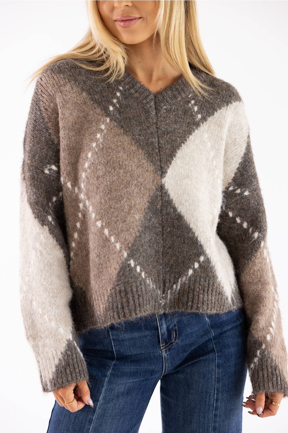 Front view of a woman wearing a brown Miracle argyle V-neck sweater featuring a soft fuzzy knit fabric and an all-over diamond pattern, paired with dark denim jeans.