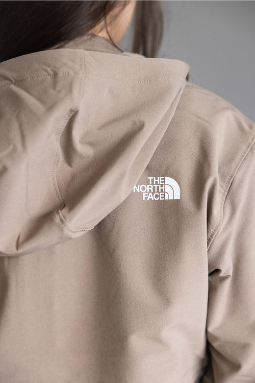 Close-up back view of a person wearing a light beige hooded jacket with a white The North Face logo on the upper back, against a plain gray background.