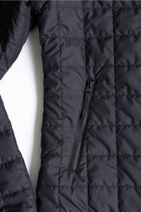 Close-up of a black quilted puffer jacket showing the texture, horizontal stitching, and a vertical zippered pocket.