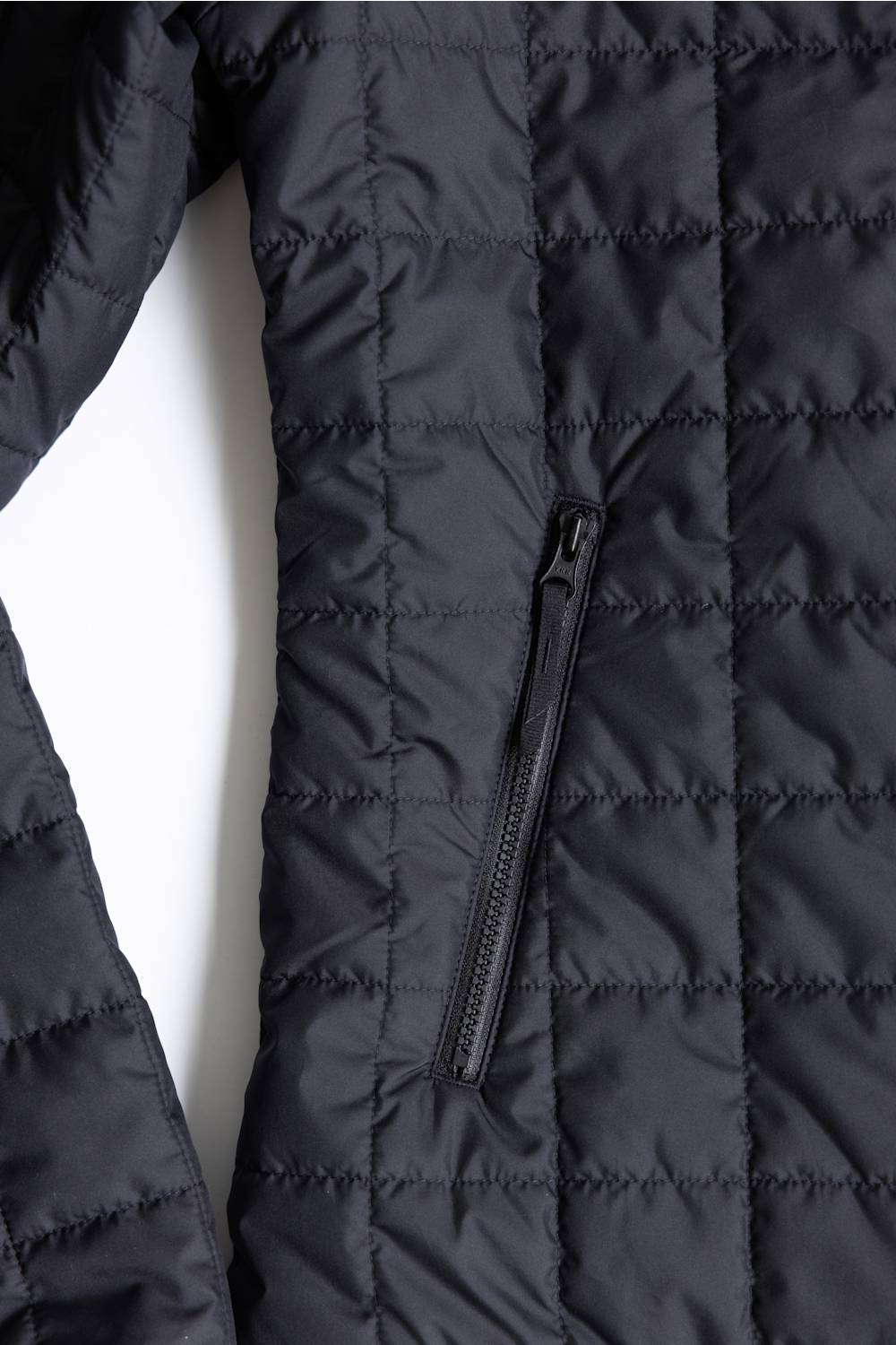 Close-up of a black quilted puffer jacket showing the texture, horizontal stitching, and a vertical zippered pocket.