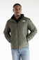 A man wearing an olive green puffer jacket by The North Face, styled with a black hoodie and blue jeans, photographed against a plain white studio background.