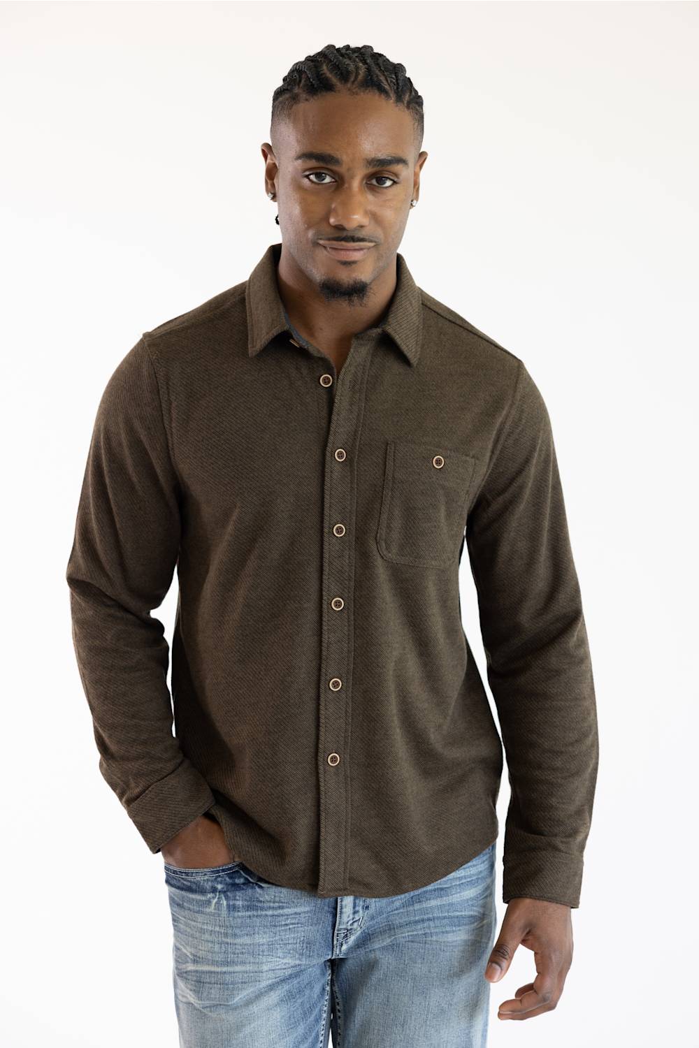 A man wearing a dark brown long-sleeve button-up shirt with a chest pocket and light blue jeans, standing against a plain white background.