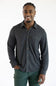 A smiling man wearing a dark charcoal gray long-sleeve button-up shirt with brown buttons and dark green pants, standing against a plain white studio background.