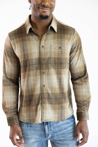 A man wearing a brown and beige plaid long-sleeve button-down shirt with blue jeans, shown from the waist up against a plain white background.