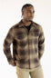 A man wearing a brown and beige plaid button-up shirt over a black t-shirt and khaki pants, photographed against a plain white background.
