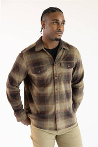A man wearing a brown and beige plaid button-up shirt over a black t-shirt and khaki pants, photographed against a plain white background.