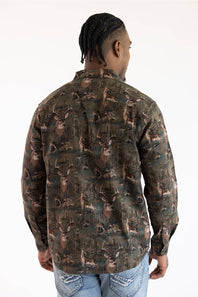 A man viewed from the back wearing a long-sleeve button-up shirt with an all-over deer camouflage pattern in shades of brown, green, and black, paired with blue jeans against a plain white background.