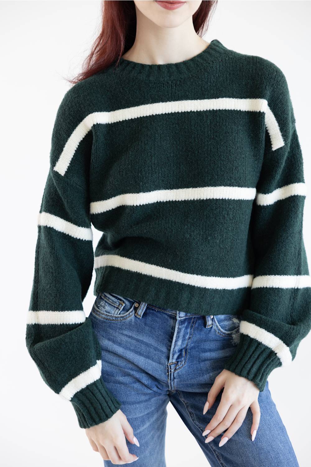 A woman wearing a dark forest green knit sweater with horizontal cream-white stripes and blue jeans, shown from the neck down against a plain white background.