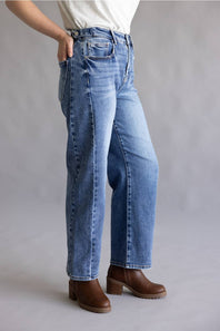 Close-up of a person's hands adjusting the waistband and button of blue denim jeans, wearing a light gray heathered t-shirt.