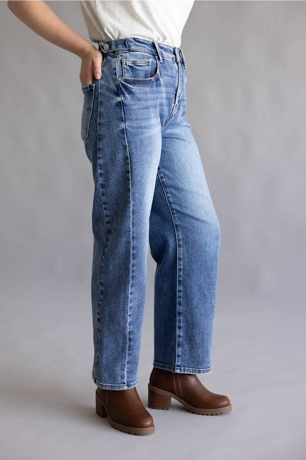 Close-up of a person's hands adjusting the waistband and button of blue denim jeans, wearing a light gray heathered t-shirt.