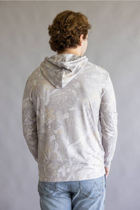 A person viewed from the back wearing a light gray hooded sweatshirt with a subtle abstract print and light blue jeans, standing against a plain gray studio background.