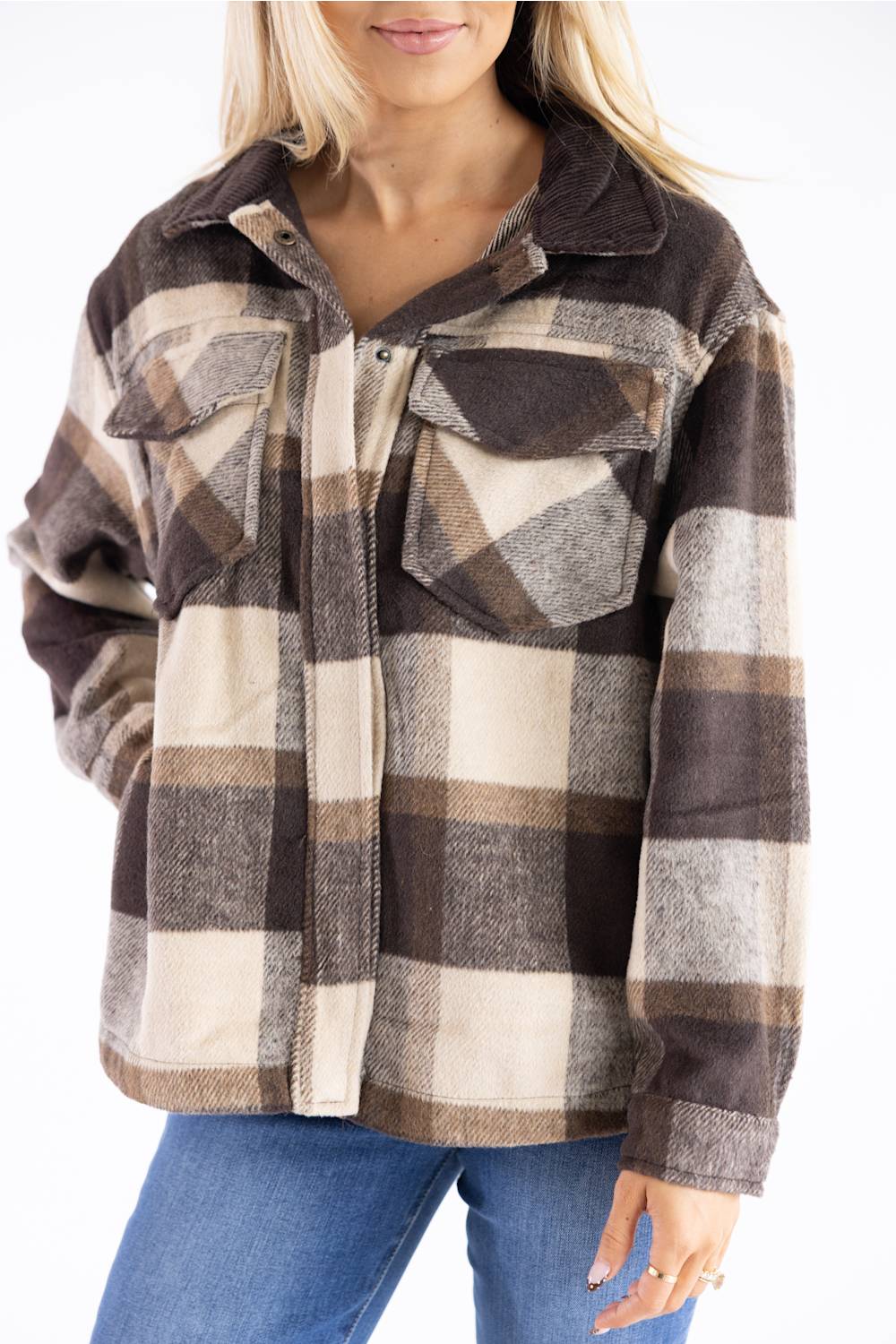 A woman wearing a brown, beige, and gray plaid button-up flannel shirt jacket with a corduroy collar, paired with blue jeans.
