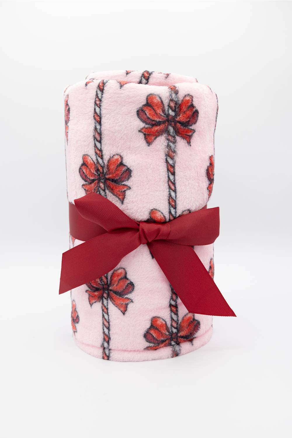 A light pink fleece blanket with a red and black bow and rope pattern, wrapped in a dark red satin ribbon bow, set against a plain white background.