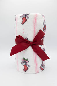 A white fleece blanket with pink stripes and red Christmas stocking patterns, tied with a dark red satin ribbon bow, shown on a white background.