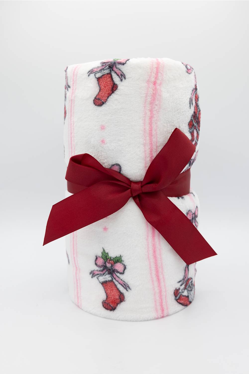 A white fleece blanket with pink stripes and red Christmas stocking patterns, tied with a dark red satin ribbon bow, shown on a white background.