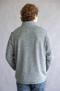 A person viewed from the back wearing a heather gray quarter-zip pullover sweater and blue jeans, standing against a plain light gray studio background.