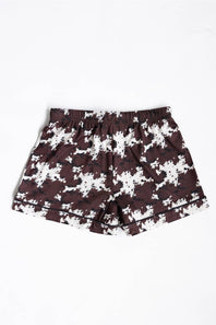 A pair of youth girls shorts featuring a dark brown and white cow pattern, with a black drawstring at the elastic waistband, laid flat against a white background.