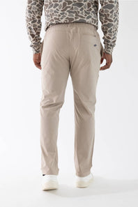 A person shown from the back wearing light beige straight-leg trousers, a beige and gray patterned long-sleeve shirt, and white sneakers against a plain white studio background.