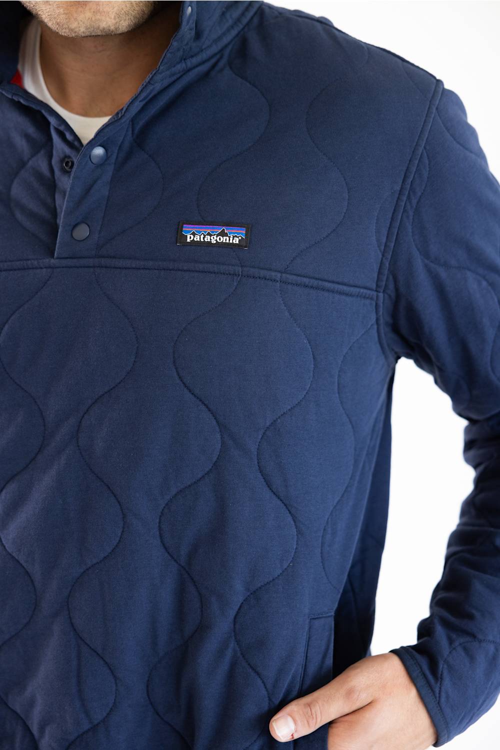 A man wearing a navy blue Patagonia quilted pullover jacket with a stand collar and zippered chest pocket, paired with blue jeans, against a plain white studio background.