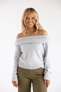 Waist-up front view of a smiling blonde model wearing the Pink Rose heather grey off-the-shoulder knit sweater, showing the wide ribbed fold-over neckline, long ribbed cuffs, and ribbed bottom hem.