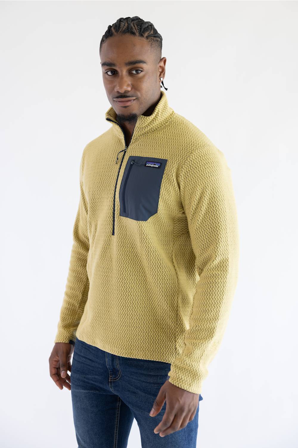 A man wearing a textured yellow quarter-zip fleece pullover with a dark navy chest pocket, paired with blue jeans, photographed against a plain white studio background.