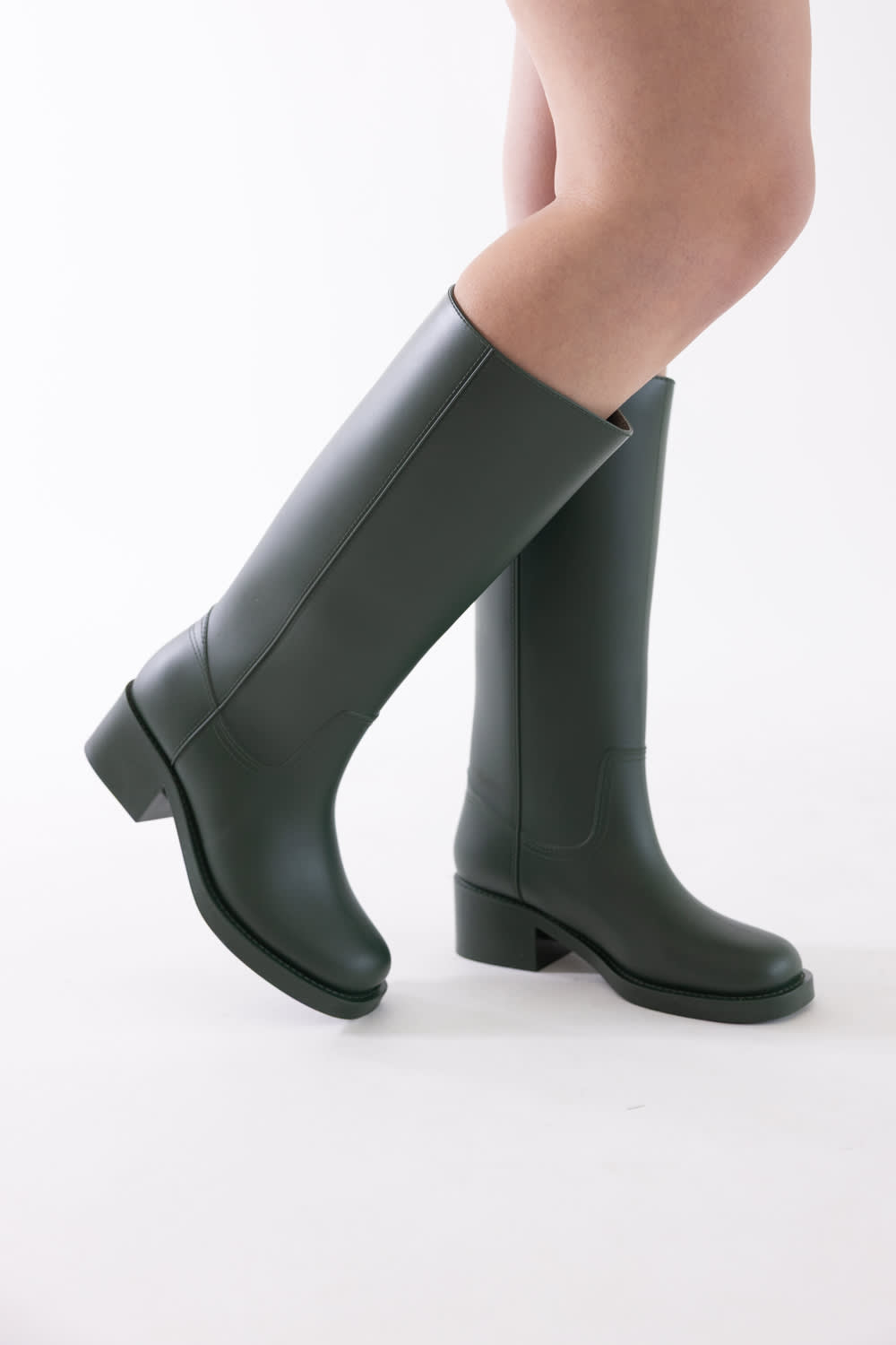 A pair of knee-high dark green rain boots worn on a model's legs, shown against a clean white studio background.